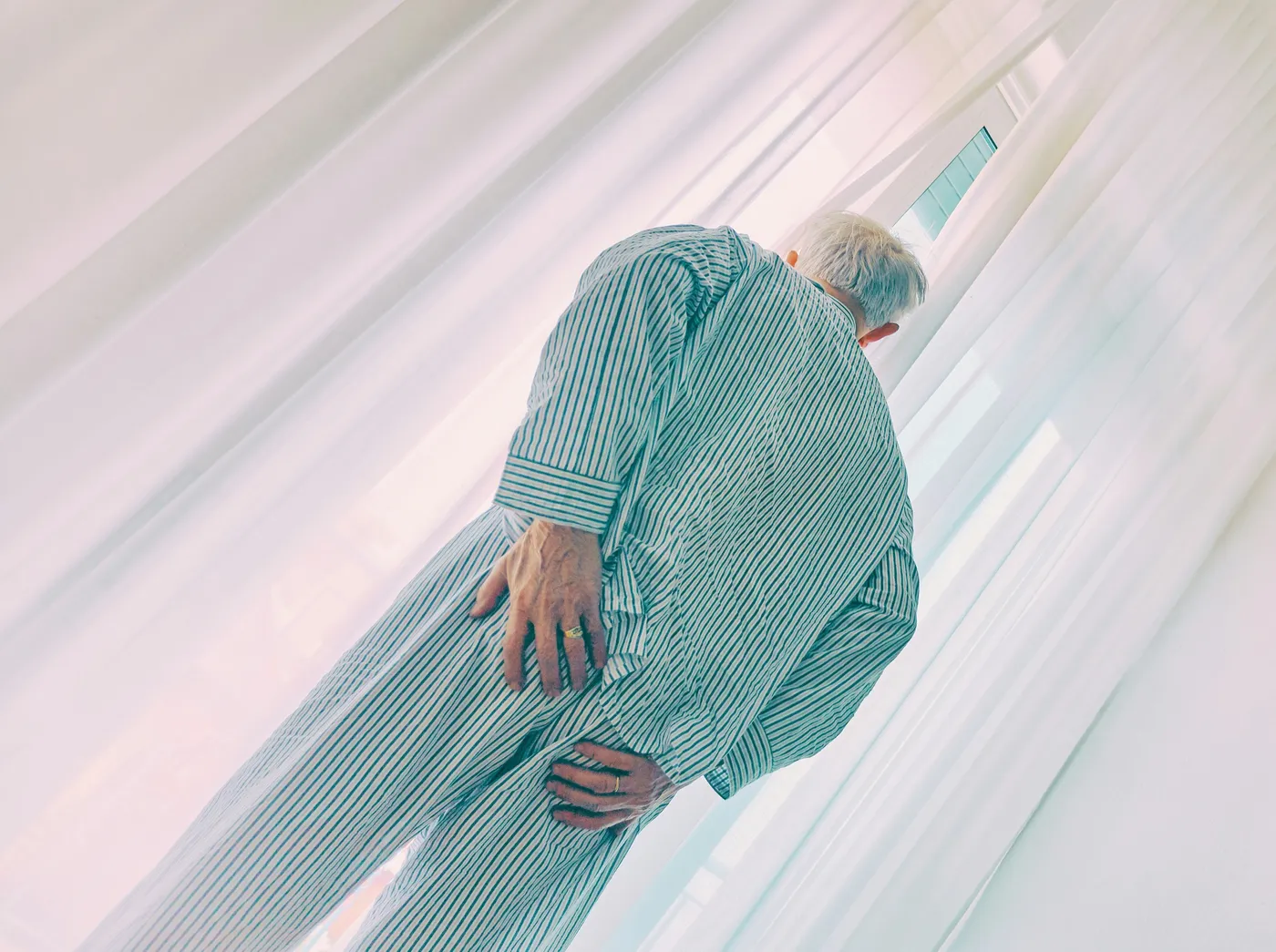 An older person in striped pyjamas bending forward with both hands resting on their thigh